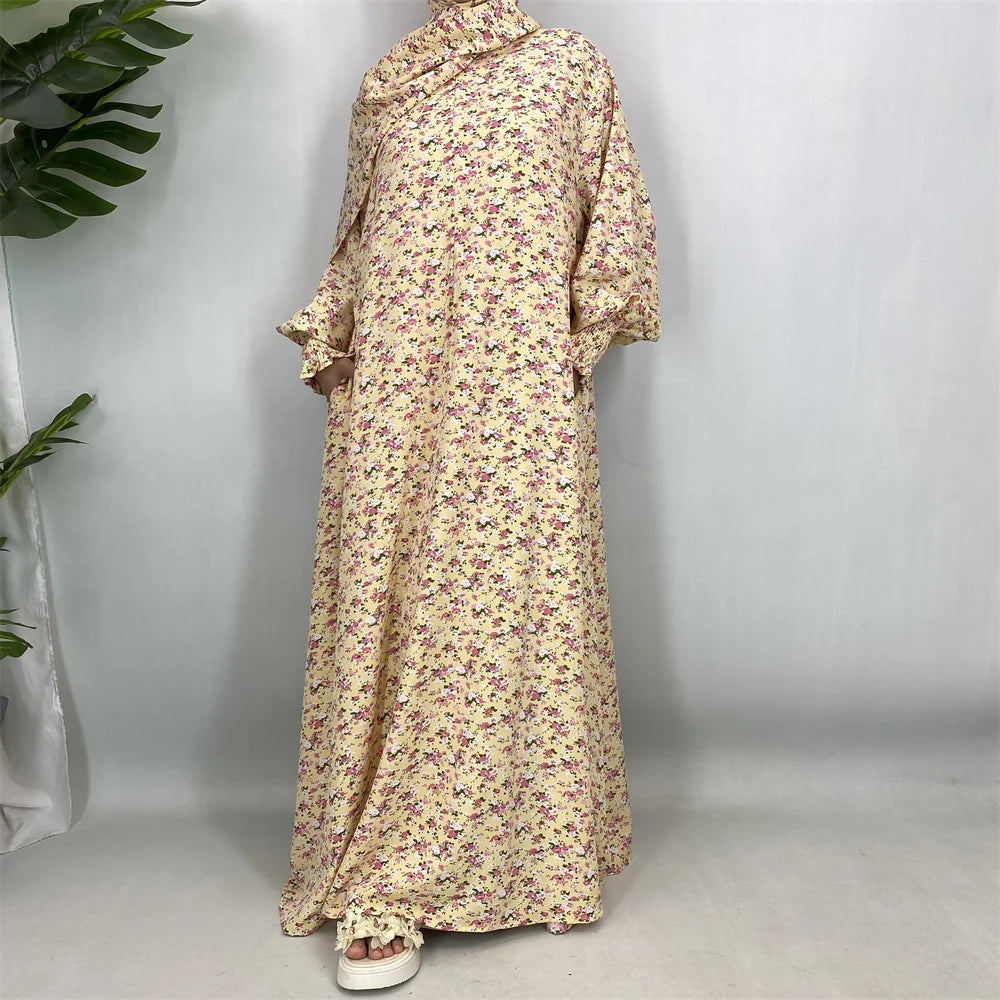 Una caftán abaya de estampado floral largo y fluido en tonos amarillo pálido y púrpura, mostrada en percha.