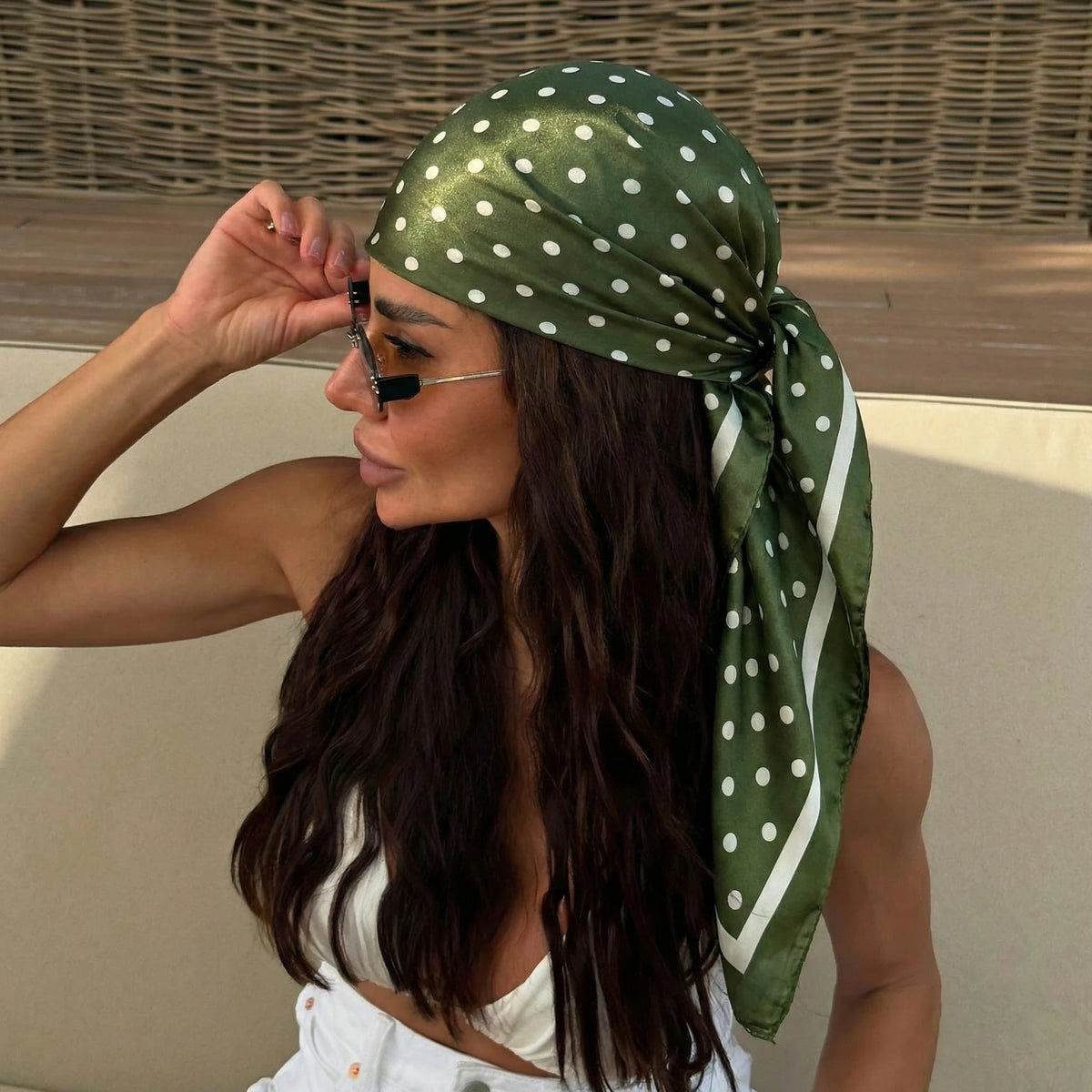A woman wearing an elegant silk dot print scarf tied around her hair, looking to the side.