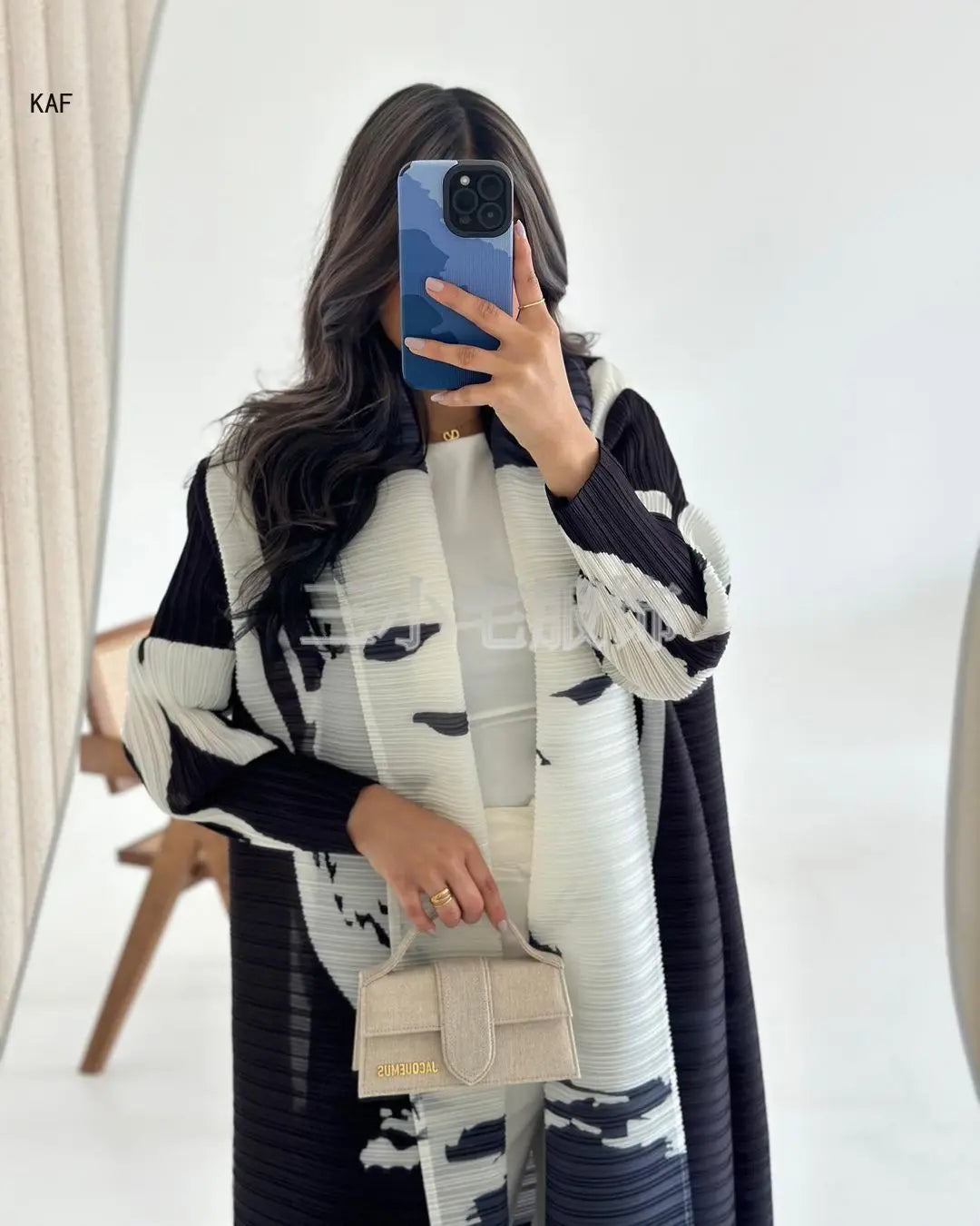Une femme modélise une veste coupe-vent plissée imprimée noir et blanc rétro et un sac beige.