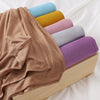 Ein Stapel von Jersey-Hijabs in verschiedenen Farben wie blau, gelb, rosa und lila, auf einem Holzständer