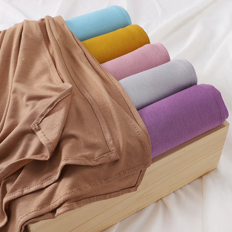 Ein Stapel von Jersey-Hijabs in verschiedenen Farben wie blau, gelb, rosa und lila, auf einem Holzständer