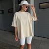 Una mujer viste una camiseta básica de algodón oversize color crema y pantalones blancos frente a una puerta de garaje gris.