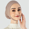 Une femme portant un foulard hijab beige uni et un haut blanc, regardant directement l'appareil photo.