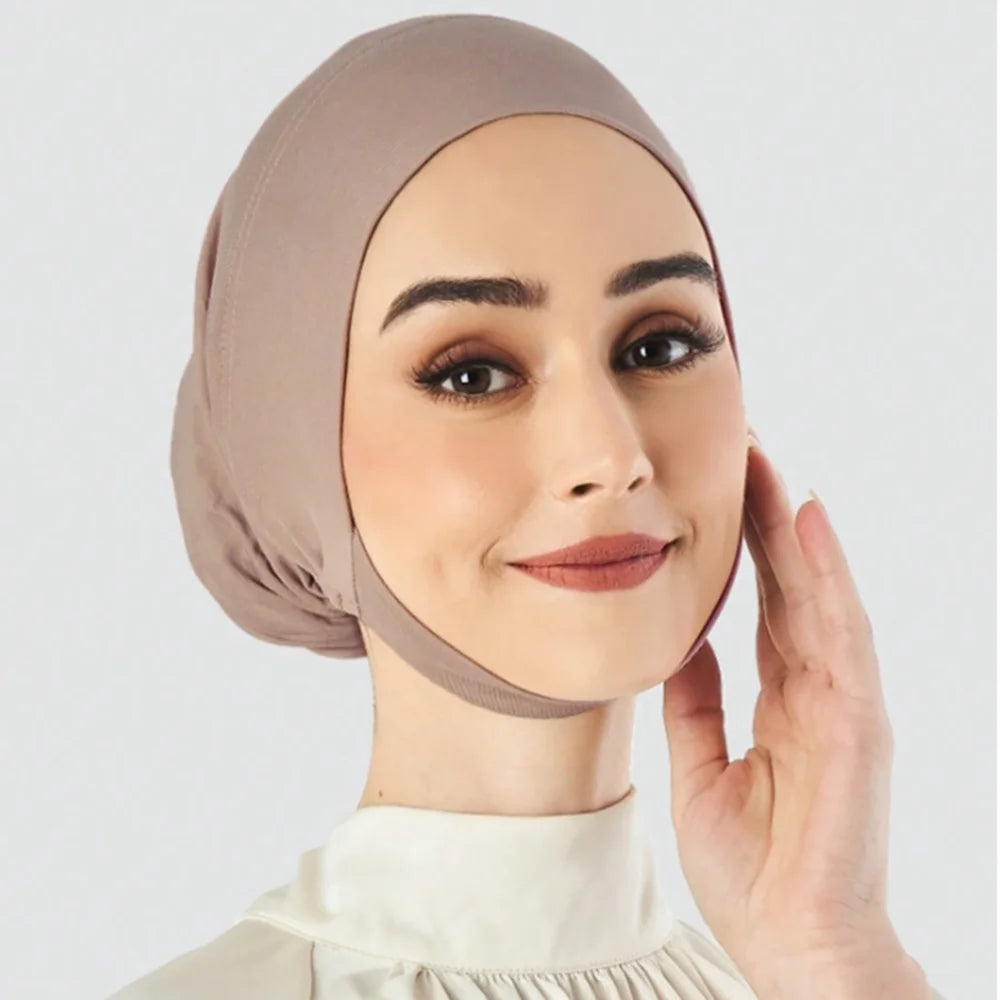Une femme portant un foulard hijab beige uni et un haut blanc, regardant directement l'appareil photo.