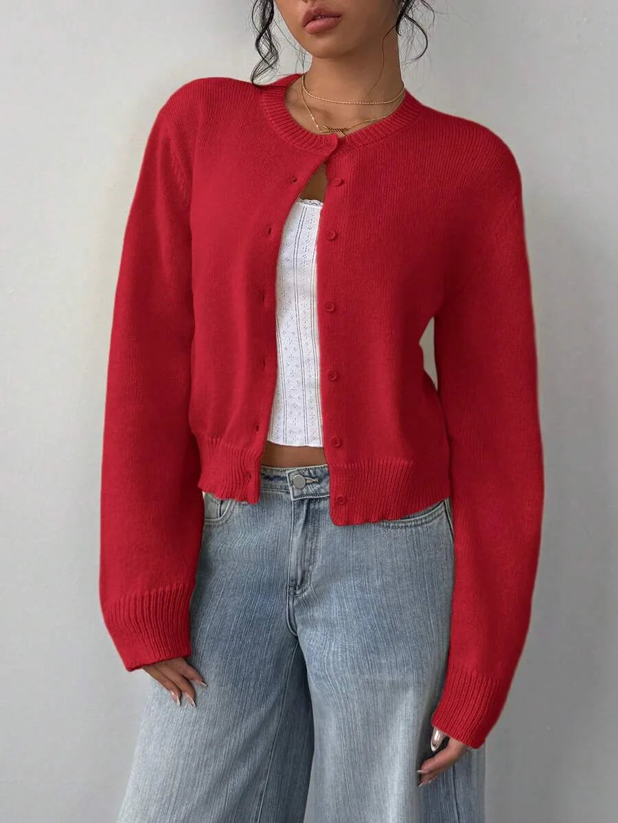 Une femme portant un pull tricoté rouge par-dessus un haut blanc et un jean bleu.
