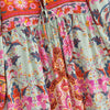 Primer plano de un vestido maxi floral bohemio con patrones rosa, naranja y verde y detalles de cordones.