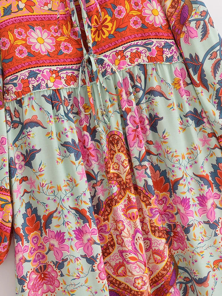 Primer plano de un vestido maxi floral bohemio con patrones rosa, naranja y verde y detalles de cordones.