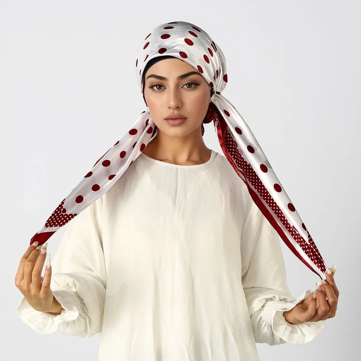 Eine Frau trägt ein weißes Oberteil und einen rot-weißen gepunkteten Satin-Instant-Hijab-Schal, der um ihren Kopf gebunden is