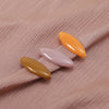A set of four solid color, elongated brooch pins in shades of orange and pink are displayed on a light pink fabric.