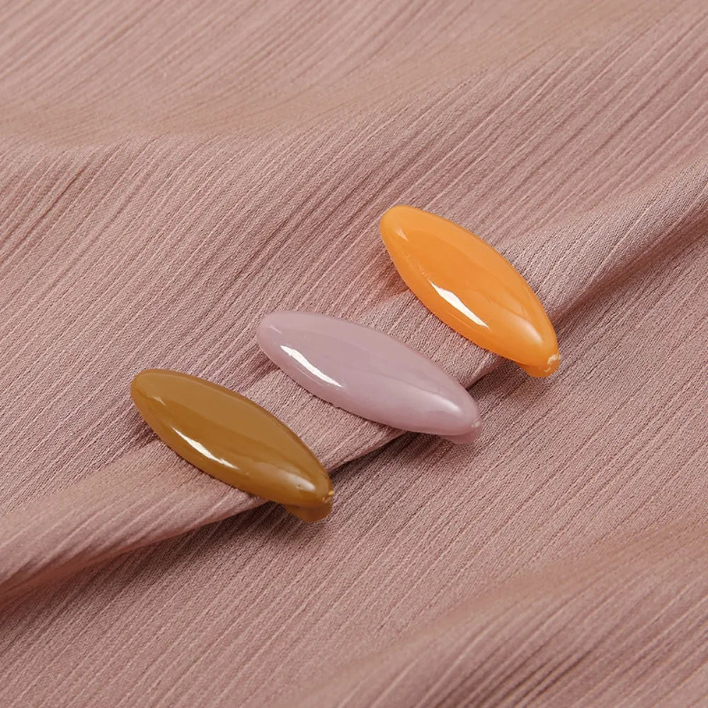 A set of four solid color, elongated brooch pins in shades of orange and pink are displayed on a light pink fabric.