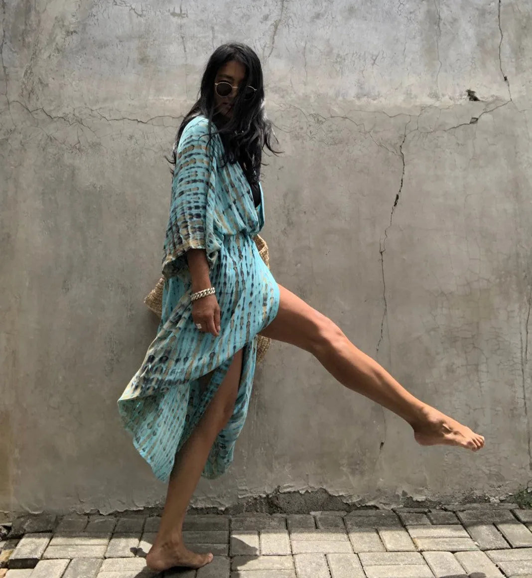 Eine Frau in einem hellblauen gemusterten Kimono-Überkleid posiert vor einer strukturierten grauen Wand.