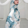A woman wearing an elegant watercolor print modal scarf in blue and white tones, draped over her head.
