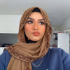 Une femme portant un hijab de mousseline marron avec un bord en dentelle de cils et un haut bleu.