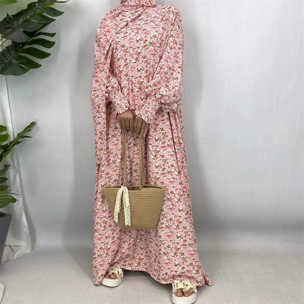 Una mujer vistiendo una kaftan abaya floral rosa de manga larga y un bolso de paja tejido.