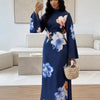 Eine Frau modelliert ein marineblaues Abaya-Kleid mit großen floralen Mustern in rosa und blau vor hellem Hintergrund.