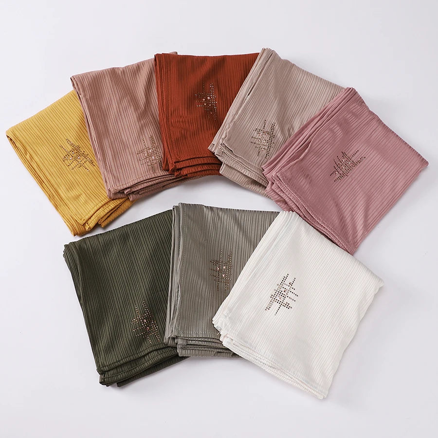 Eine Kollektion von geriffelten Jersey-Hijab-Schals in verschiedenen Farbtönen wie Senffarben, Terrakotta, Beige und Pink.