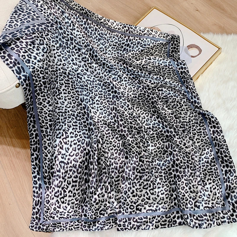 A black and white leopard print silk satin neckerchief hijab scarf draped on a light surface.