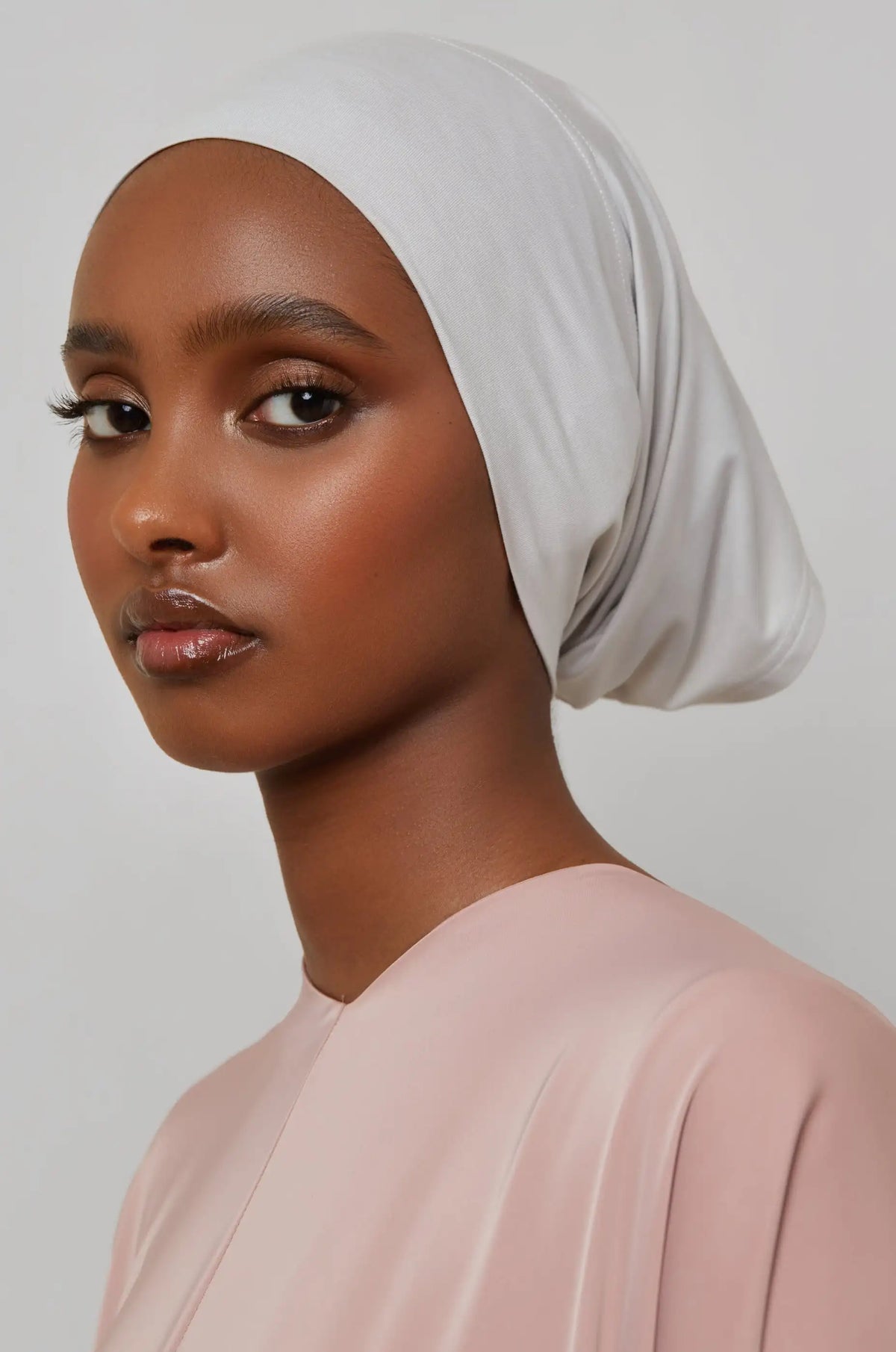 Model trägt eine hellgraue Bambus-Jersey-Turban-Kappe und ein blassrosa Oberteil.
