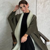 Eine Frau trägt einen langen, olivgrünen gefalteten Abaya-Cardigan über einem schwarzen Kleid.