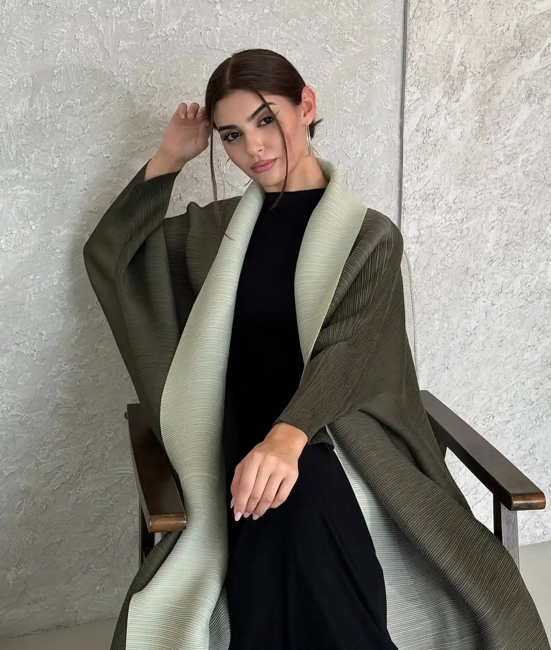 Eine Frau trägt einen langen, olivgrünen gefalteten Abaya-Cardigan über einem schwarzen Kleid.