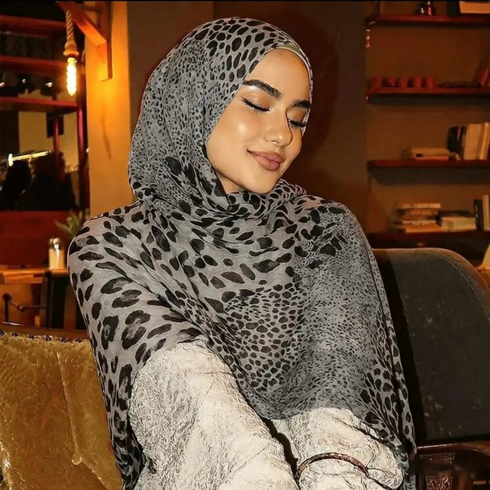 Eine Frau in grauem Leopardenmuster und gepunktetem Baumwollschal, die in die Kamera blickt.