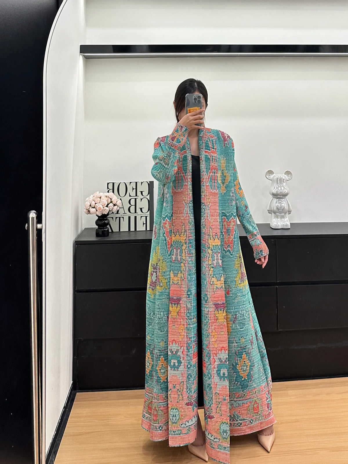 Une femme modélise une veste coupe-vent plissée à imprimé rétro bleu sarcelle et rose dans un environnement de vente moderne.