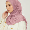 Eine Frau trägt einen einfarbigen rosa Jersey-Hijab und eine weiße strukturierte Jacke.