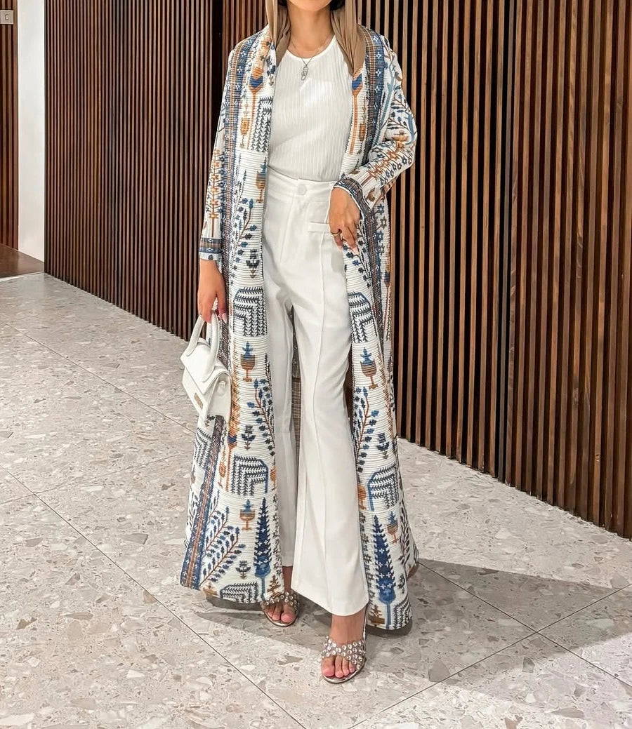 Une femme portant un haut et un pantalon blancs avec un trench-coat à manches longues plissé à motifs bleus et beige.