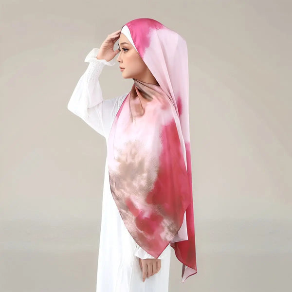 A woman wearing a pink and white tie-dye printed satin silk hijab scarf over a white outfit.