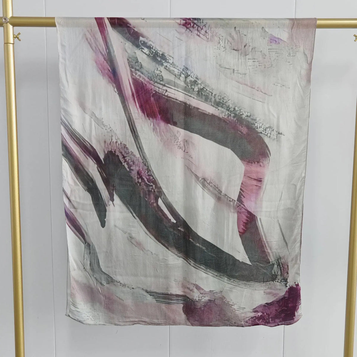 Helles graues Schal mit abstrakten violetten und rosa Streifen an einem goldenen Haken.