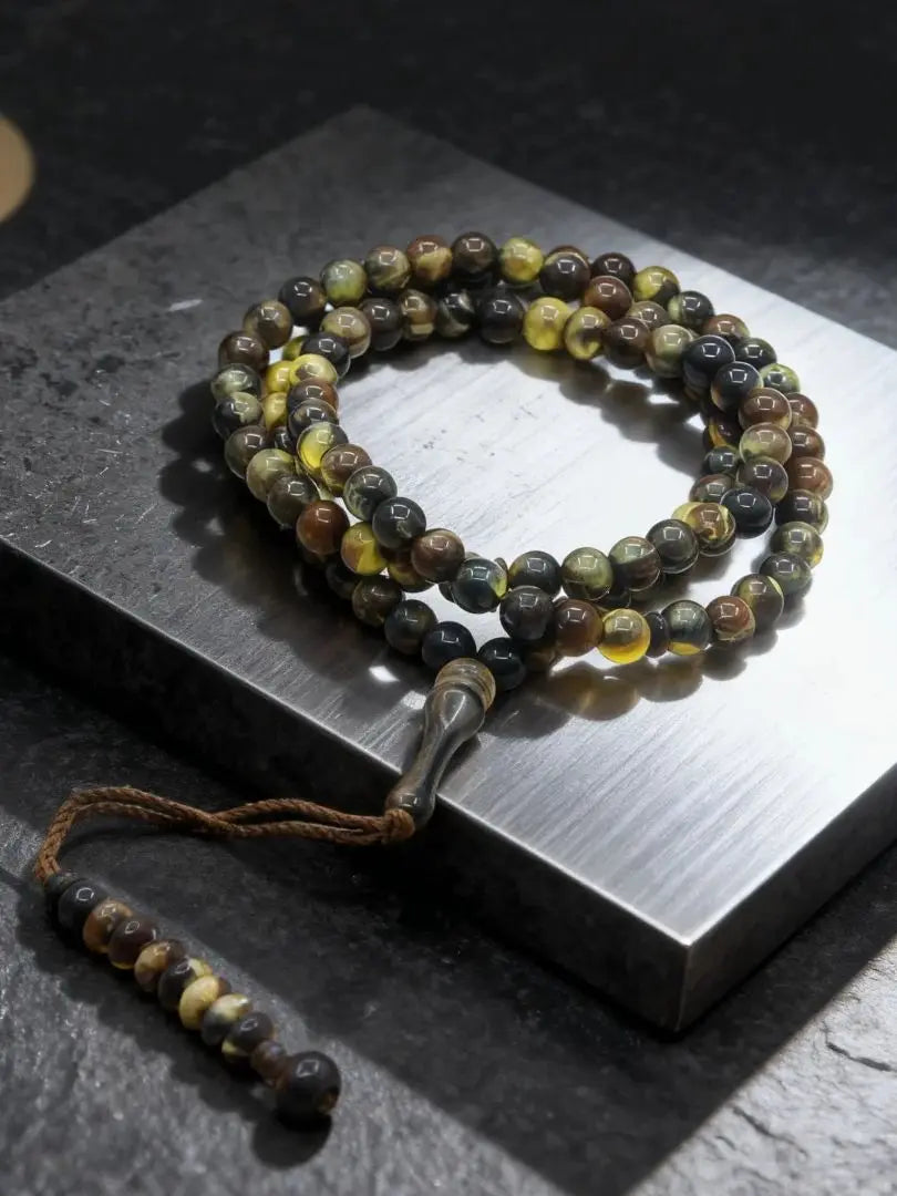 Una pulsera de cuentas oscuras y amarillas con borlas de luna y estrella sobre una superficie gris.