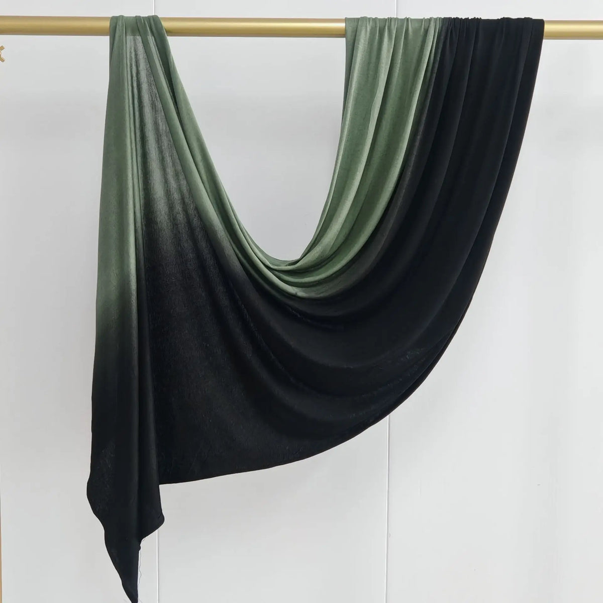Pañuelo de algodón en degradado verde oscuro y negro drapeado sobre una varilla de madera.