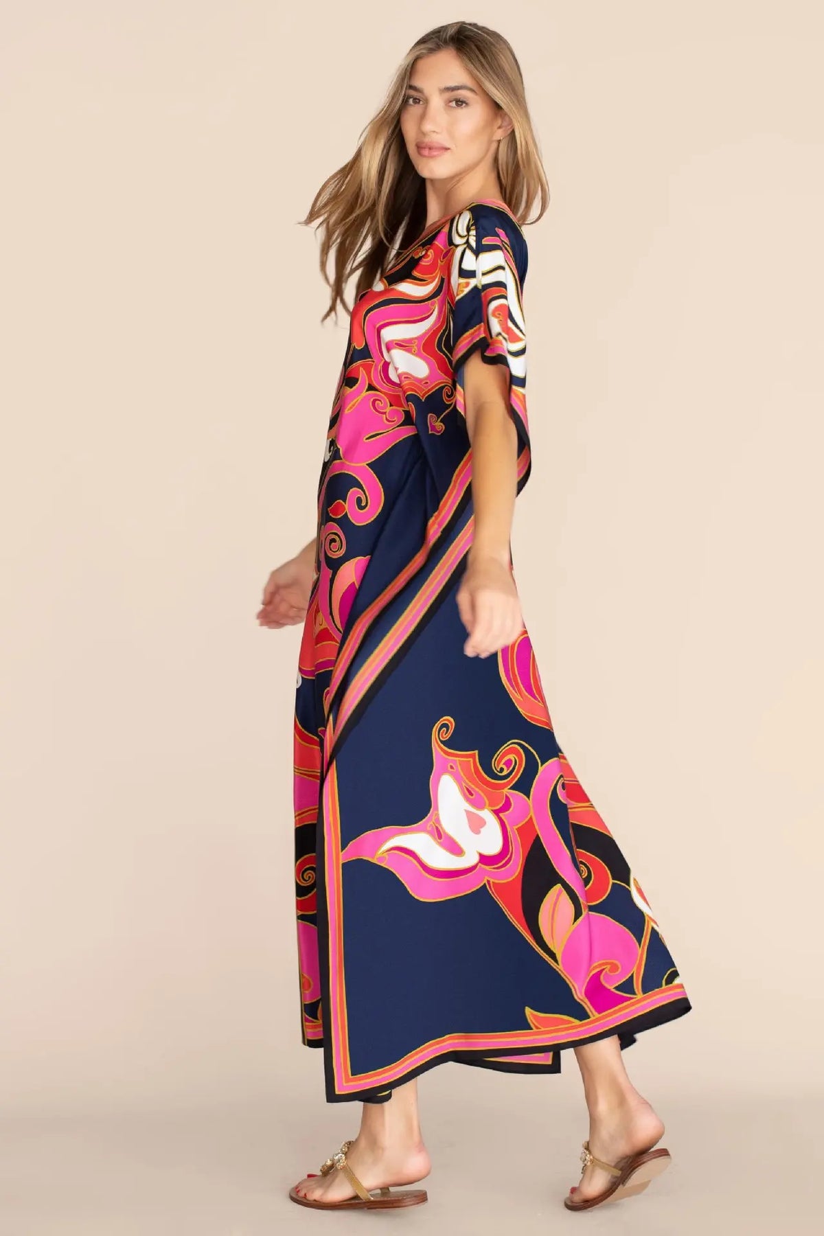 Una mujer modela un caftán de playa largo y fluido con estampado bohemio floral en azul marino y rosa.