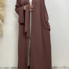 Eine Frau trägt ein fließendes, offenes Abaya-Kaftan in pudriger Rosa mit einem passenden Schal.