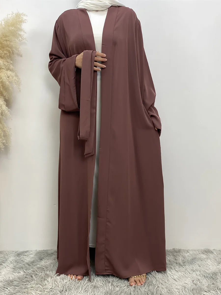 Eine Frau trägt ein fließendes, offenes Abaya-Kaftan in pudriger Rosa mit einem passenden Schal.