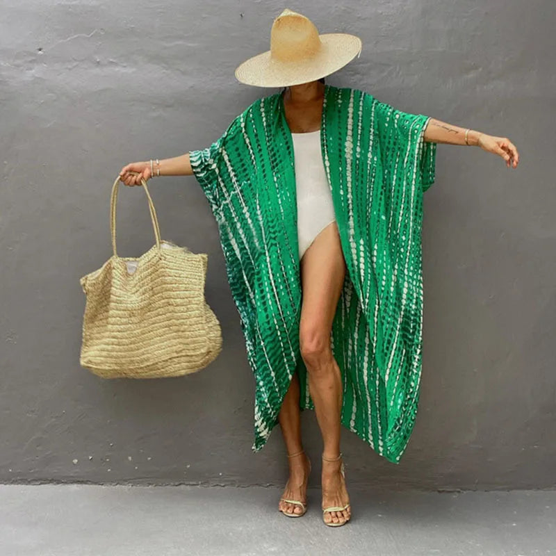 Model in a green patterned kimono cover-up over a white dress and straw hat