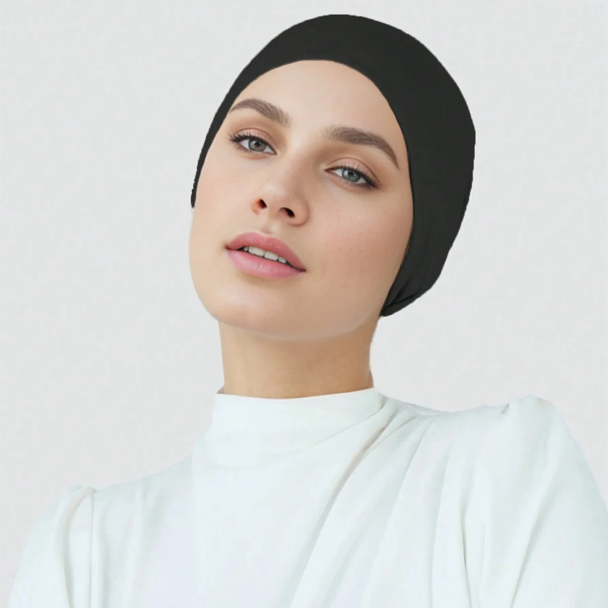 Eine Frau trägt einen schwarzen Premium-Stretch-Baumwoll-Hijab, eine Unterdecke und ein weißes Rollkragenoberteil.