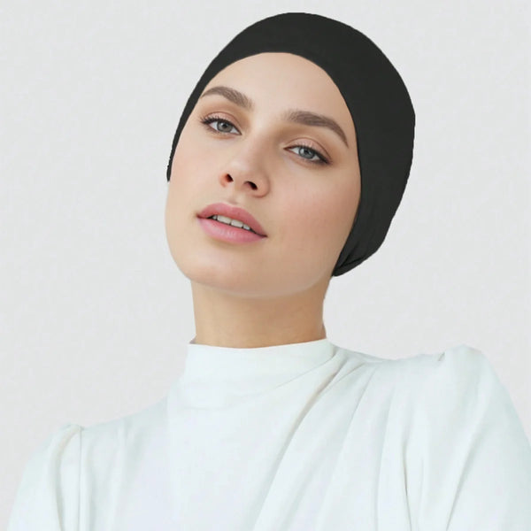 امرأة ترتدي حجاباً أسود من القطن المطاطي ووشاح وقبعة، وبلوزة بيضاء برقبة عالية.
