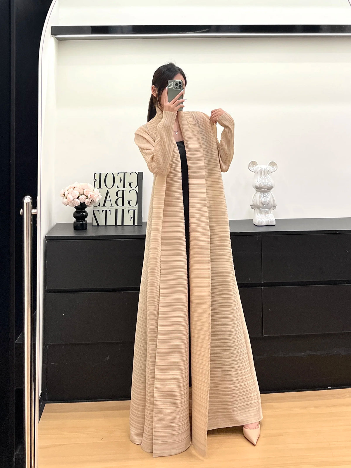 Une femme modélise une veste coupe-vent plissée beige en plan complet sur un fond noir et blanc.