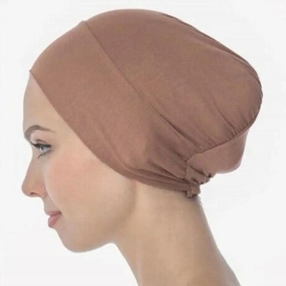 A close-up profile view of a woman wearing a dusty rose breathable cotton underscarf with an elastic fit.