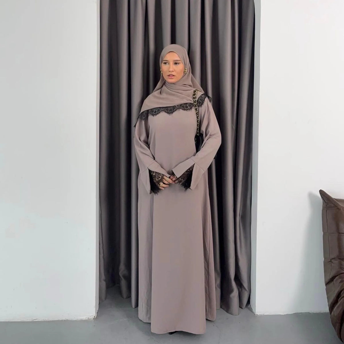 Una mujer vistiendo una abaya gris larga y modesta con detalles de encaje negro y un hiyab a juego.