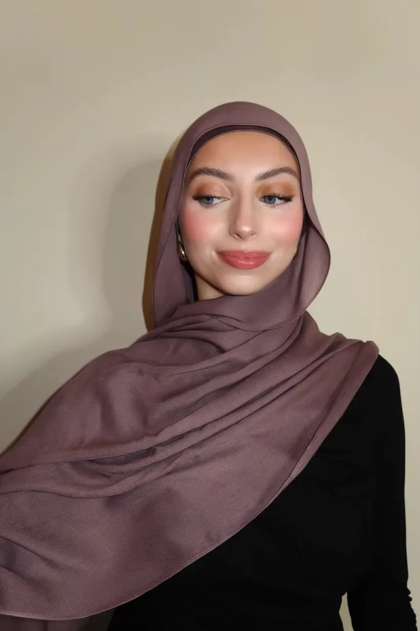 Eine Frau trägt einen mauvefarbenen Gradient-Rayon-Modal-Hijabschal und schwarze Kleidung.