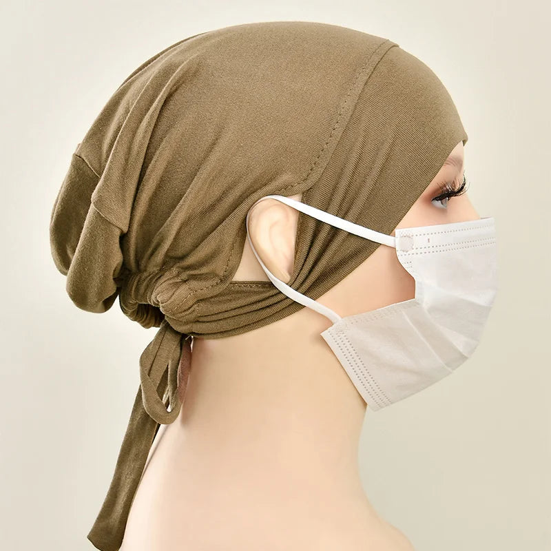 Eine Frau trägt eine olivgrüne Jersey-Baumwoll-Hijab-Kappe und eine weiße Schutzmaske.