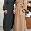 Eine Frau trägt eine lange, fließende braune marokkanische Kaftan-Abaya mit schwarzem Hijab und dunklen Hosen.