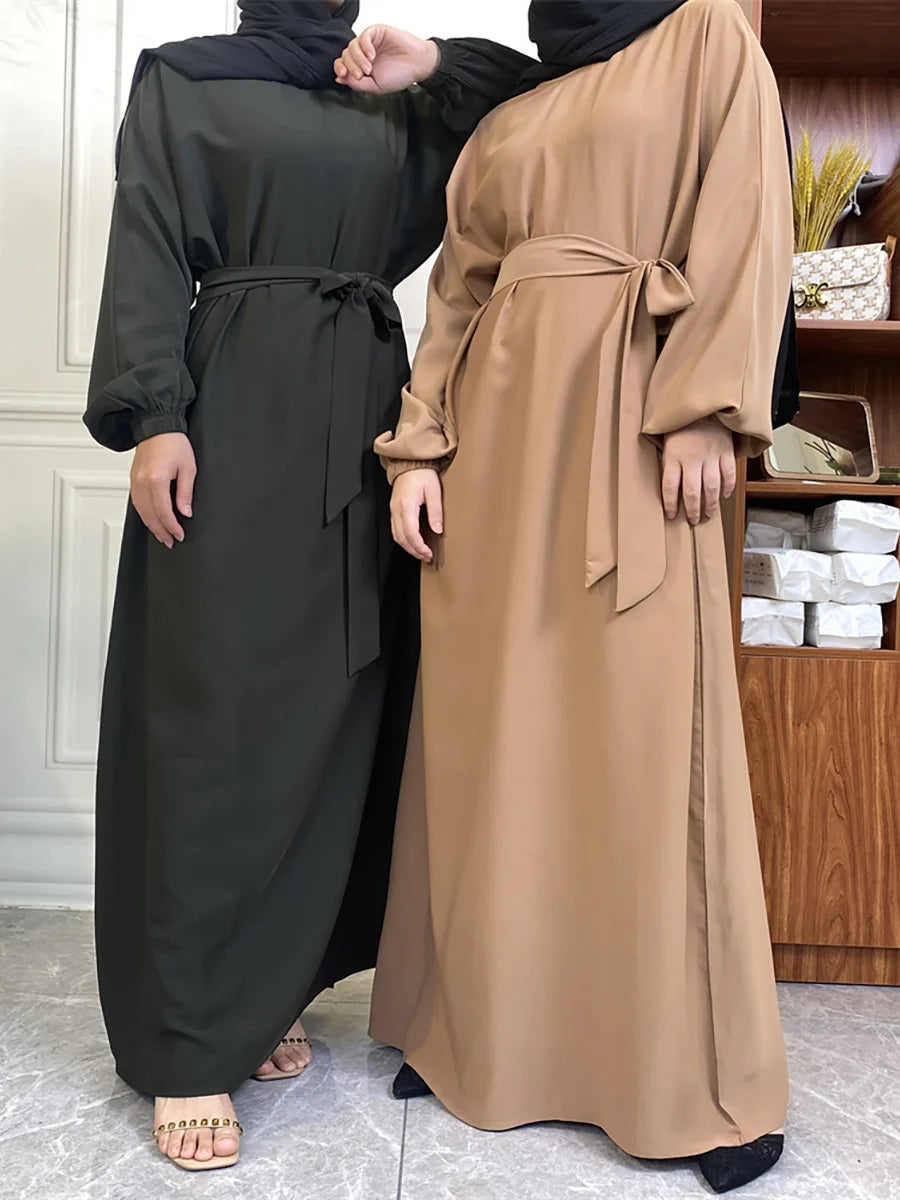Eine Frau trägt eine lange, fließende braune marokkanische Kaftan-Abaya mit schwarzem Hijab und dunklen Hosen.