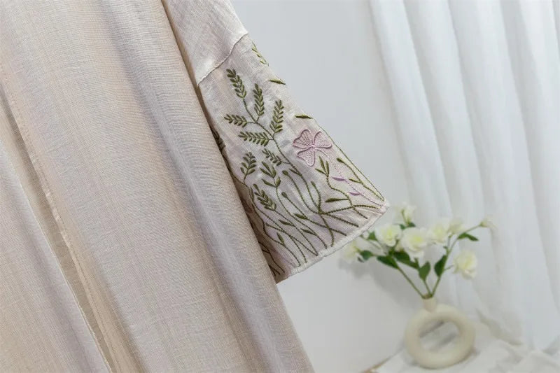 Nahaufnahme eines hellbeigen Kaftan-Abayas mit zarten grünen und lila Stickereien am Ärmel.