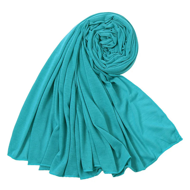 Un foulard hijab en jersey de coton bleu sarcelle roulé et drapé, montrant sa texture douce.