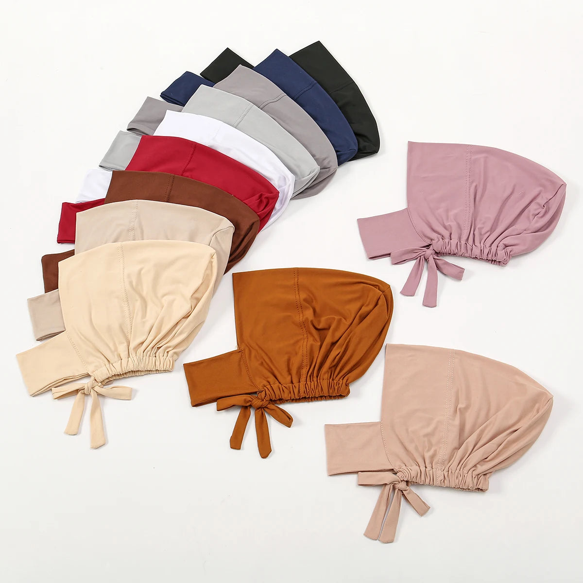 A collection of various colored inner hijab caps and scarves laid out on a white background.