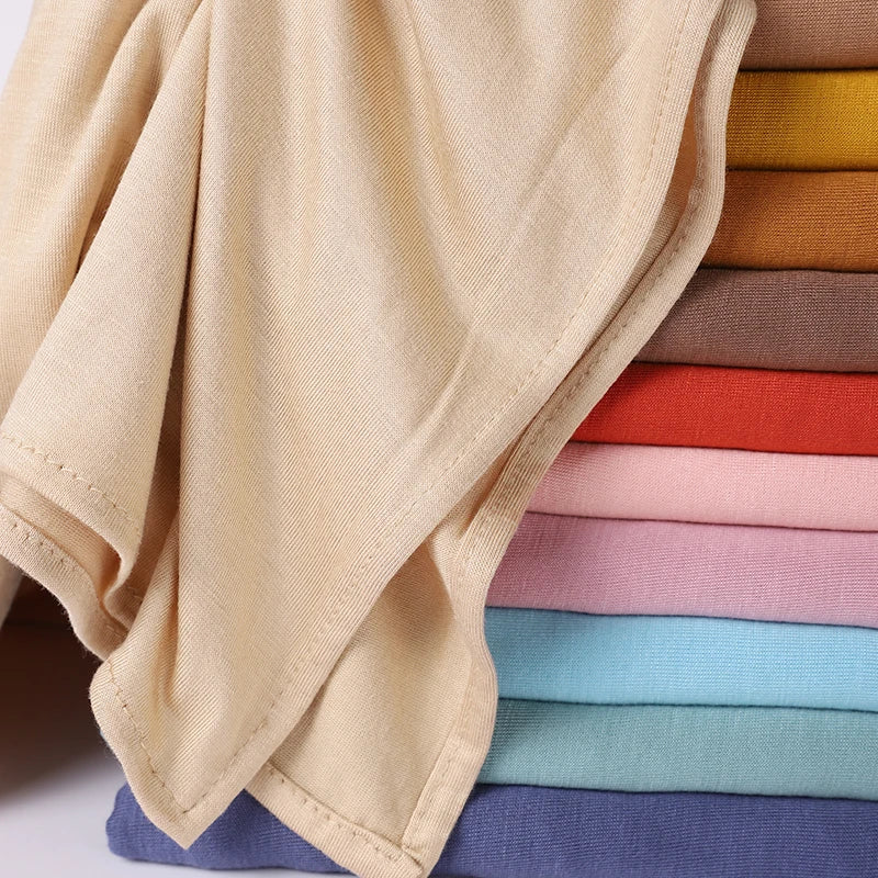 Ein Stapel weicher Baumwoll-Jersey-Instant-Hijab-Schals in verschiedenen Pastell- und Erdtönen, gefaltet und präsentiert.