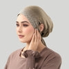 Eine Frau trägt eine beige Jersey-Baumwoll-Hijabkappe mit silbernen Verzierungen und blickt zur Seite.
